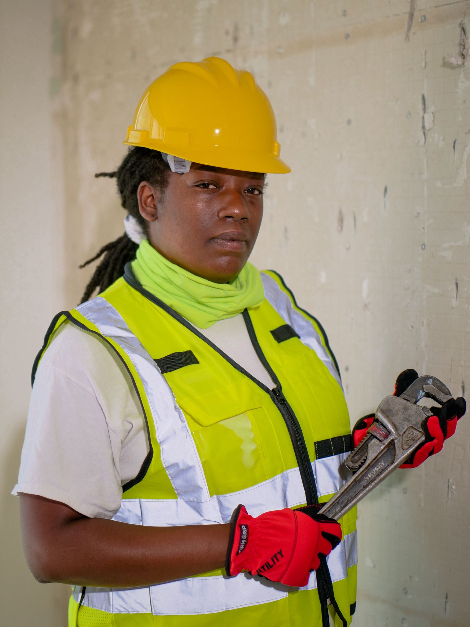 Plumber in a hard hat, safety vest and gloves holding a pipe wrench