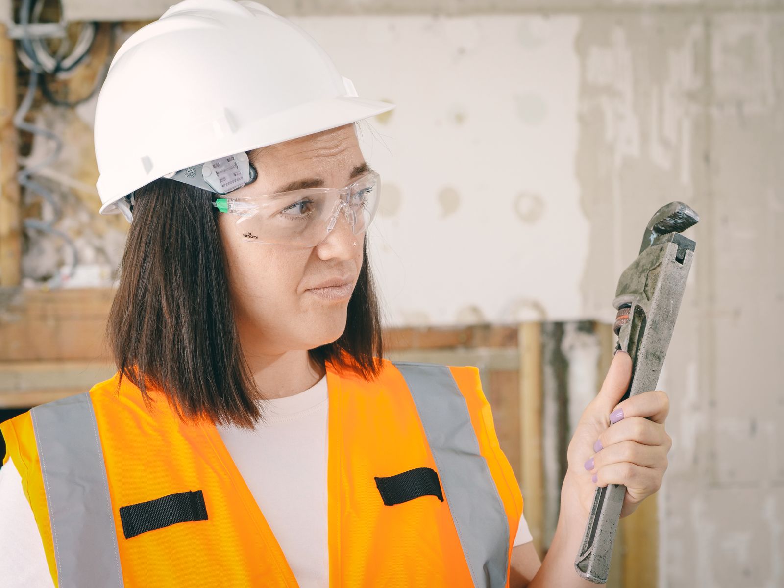 Plumber in safety gear checking a pipe wrench